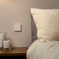 A smart switch placed strategically beside a nightstand next to a bed with pillows