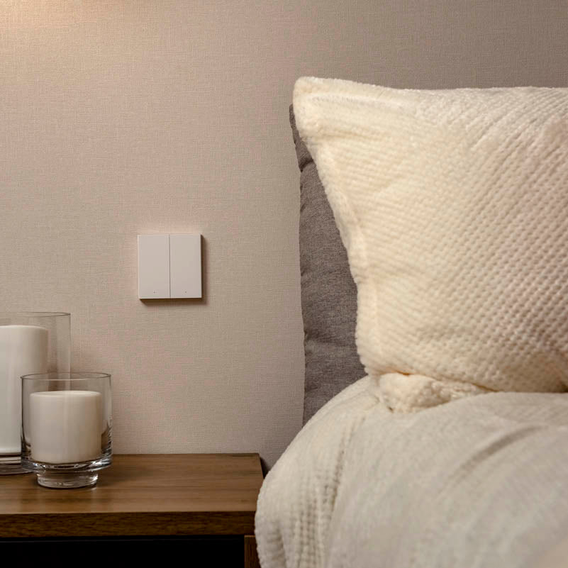 A smart switch placed strategically beside a nightstand next to a bed with pillows