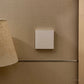 Beige lampshade on a wooden stand against a textured beige wall.