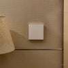 Beige lampshade on a wooden stand against a textured beige wall.