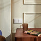 Brown mug and book on a wooden table against a beige wall with a blue pillow.