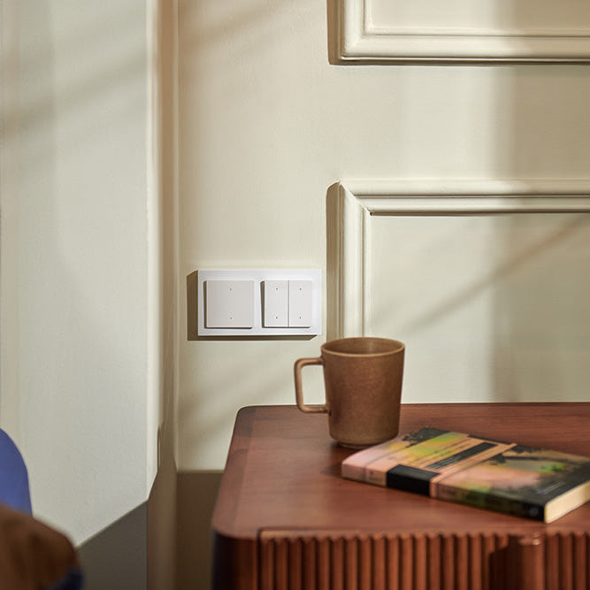 Brown mug and book on a wooden table against a beige wall with a blue pillow.