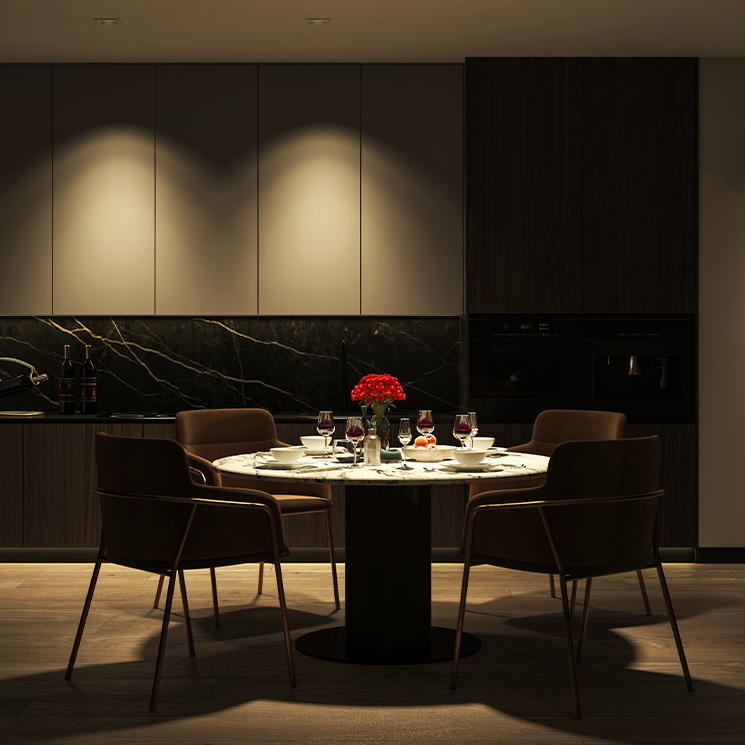 A side-by-side before and after comparison of a dining room in low light versus illuminated lighting. The left side is labeled 'Before' and is quite dark, while the right side is labeled 'After' and shows the dining table, chairs, and cabinetry more clearly with warm ambient lighting.