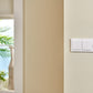 White light switch panel on a beige wall with a blurred outdoor background